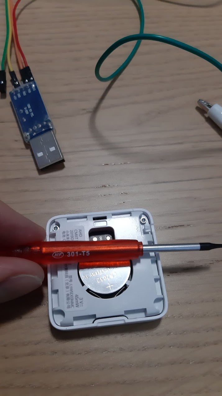 disassembled xiaomi mi BLE temperature / humidity sensor on the wooden table with T5 screwdrive over it and usb2ttl adapter in the back